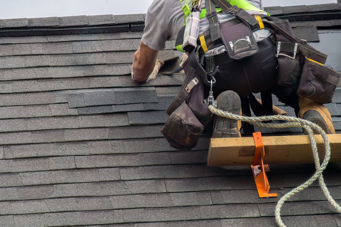 A roofer installing shingles on a job site, representing the need for general contractor insurance.