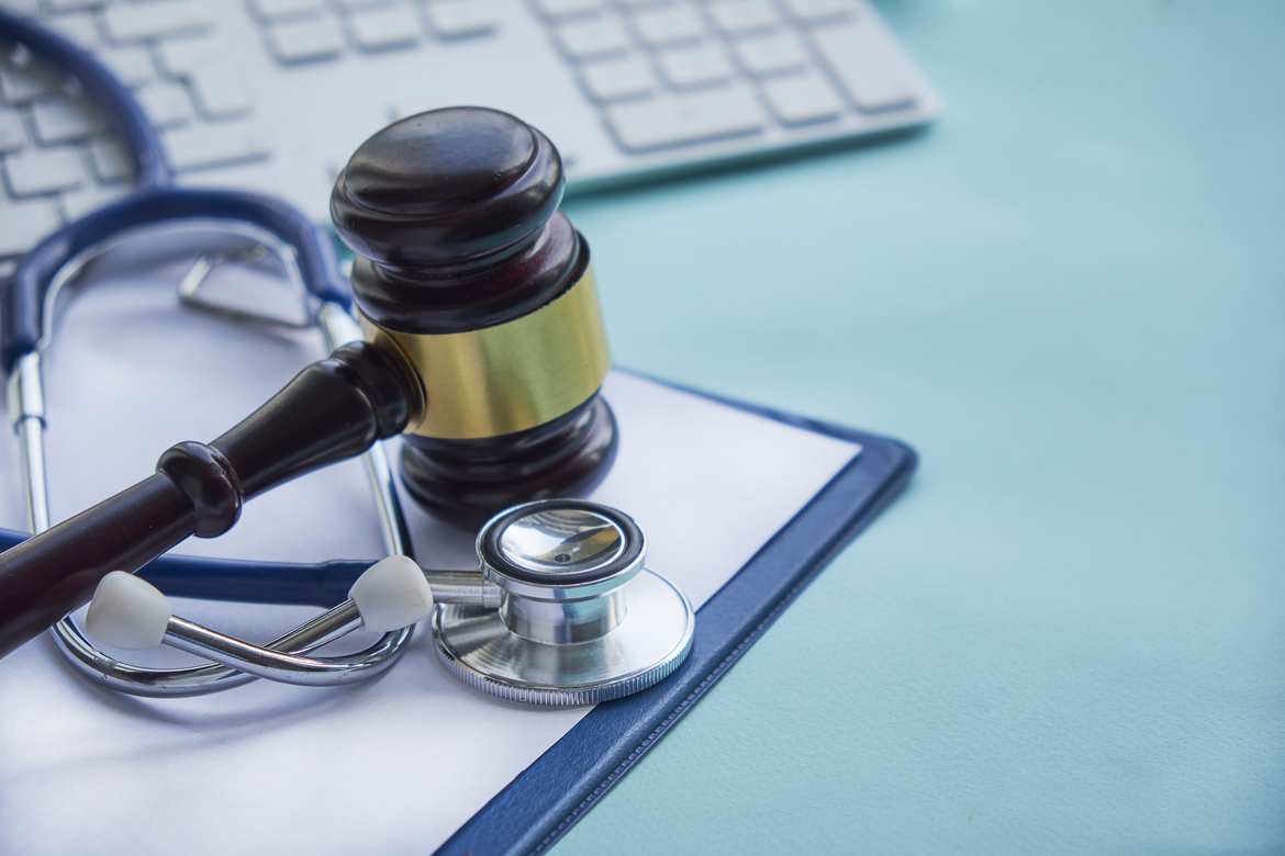 A gavel and a stethoscope rest on a clipboard in front of a computer, representing healthcare professional liability insurance