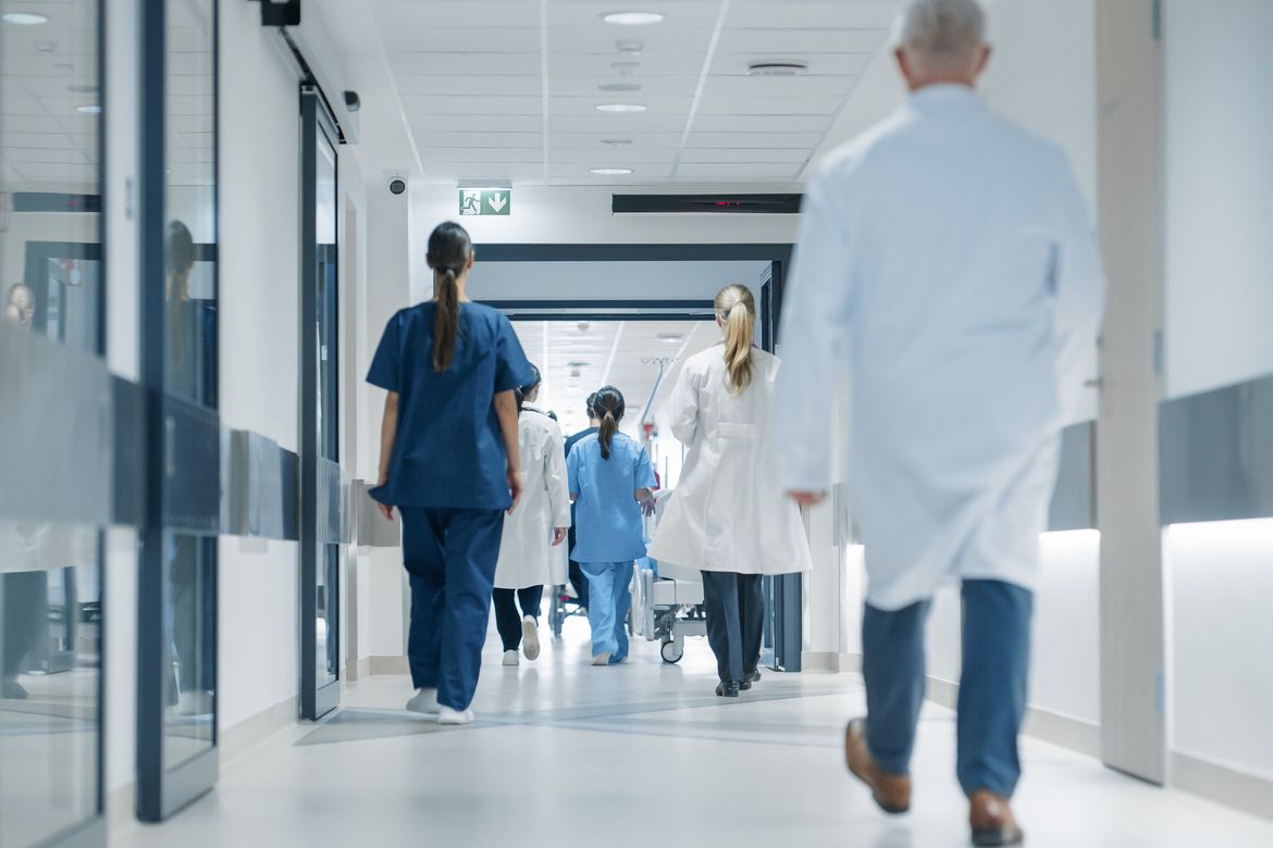 Various hospital staff walk down a hallway after a patient, representing medical practice insurance requirements.