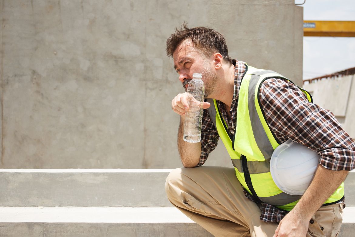 An outdoor worker drinks water on a construction site to prevent heat exhaustion & workers’ compensation claims.