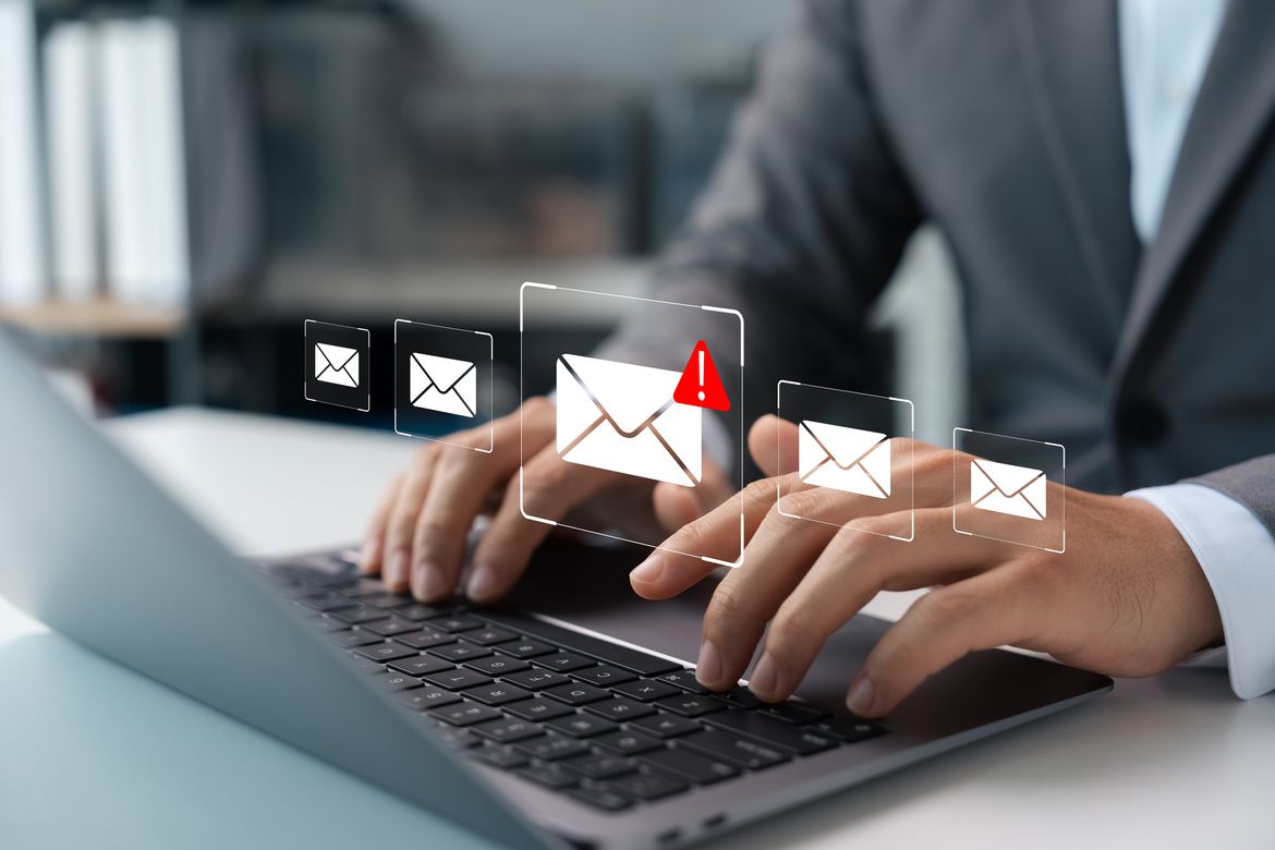 A small business owner reviews suspicious emails on a laptop, representing cybercrime and phishing risks.